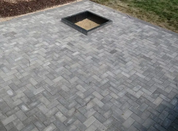 A grey herringbone paver patio with a charcoal border and a square left open for a fire pit